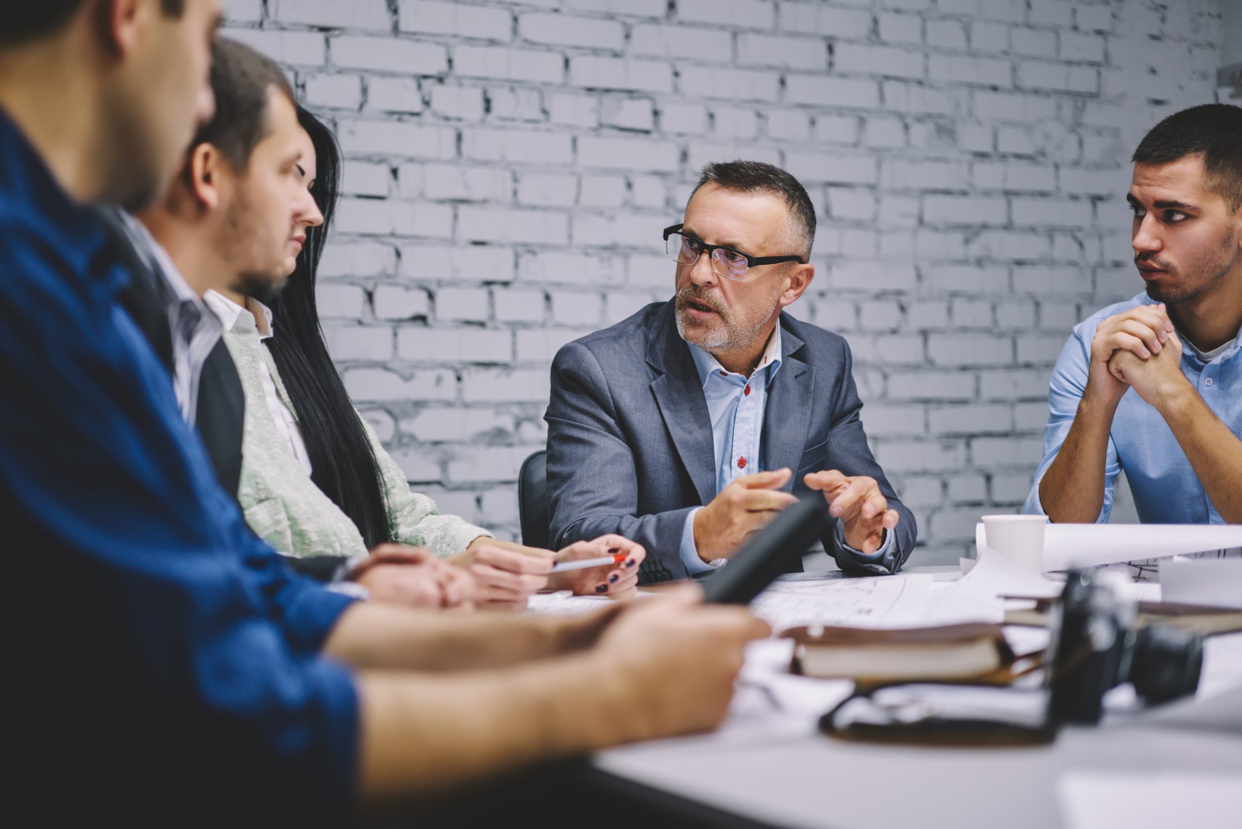 Group of executive managers discussing exchange experience and business strategy during involved briefing in office room, formally dressed male and female colleagues talking about competition